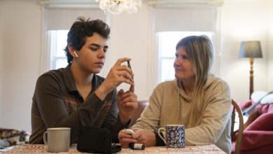 A mother supporting her teenaged diabetic son at home while he tests his blood sugar levels. Photographed in North America.